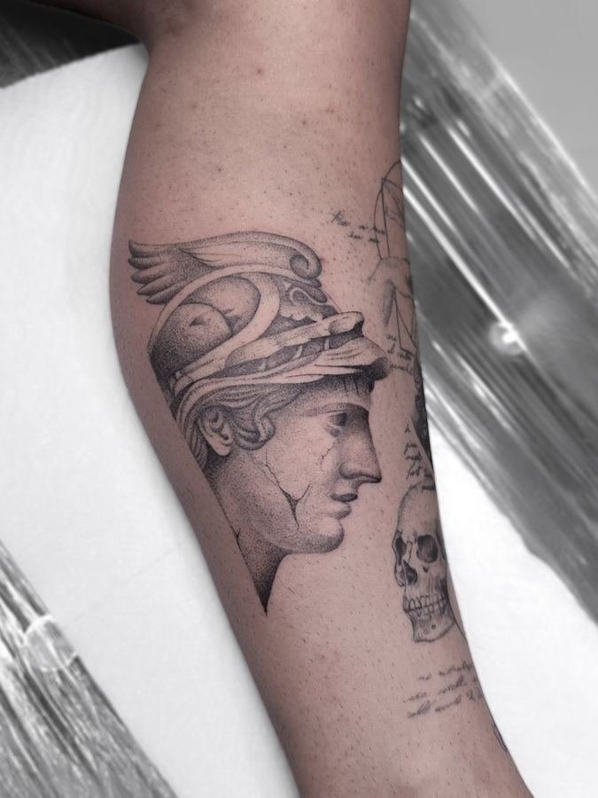 Rostro de Hermes con casco alado, estilo escultura griega, en el antebrazo