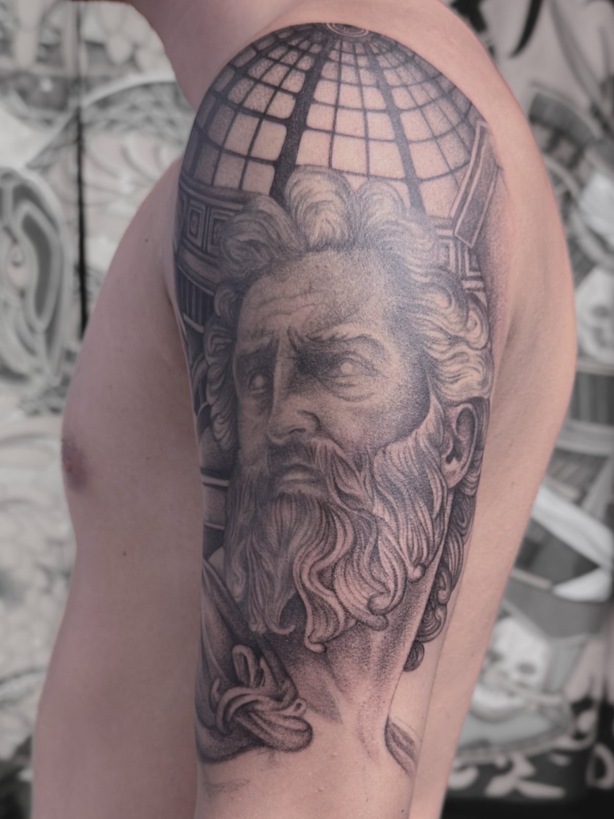 Tatuaje de Atlas cargando el mundo, en realismo negro y gris, en el brazo